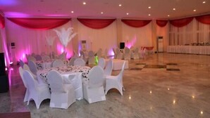 A banquet hall with round tables and white chairs, red drapes, and ceiling lights. - Karma Hotel (Lagos)
