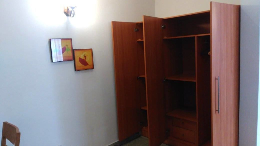 A room with a wooden wardrobe, a chair, and two framed pictures on the wall.