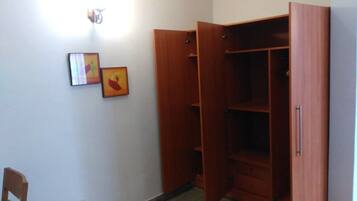 A room with a wooden wardrobe, a chair, and two framed pictures on the wall.