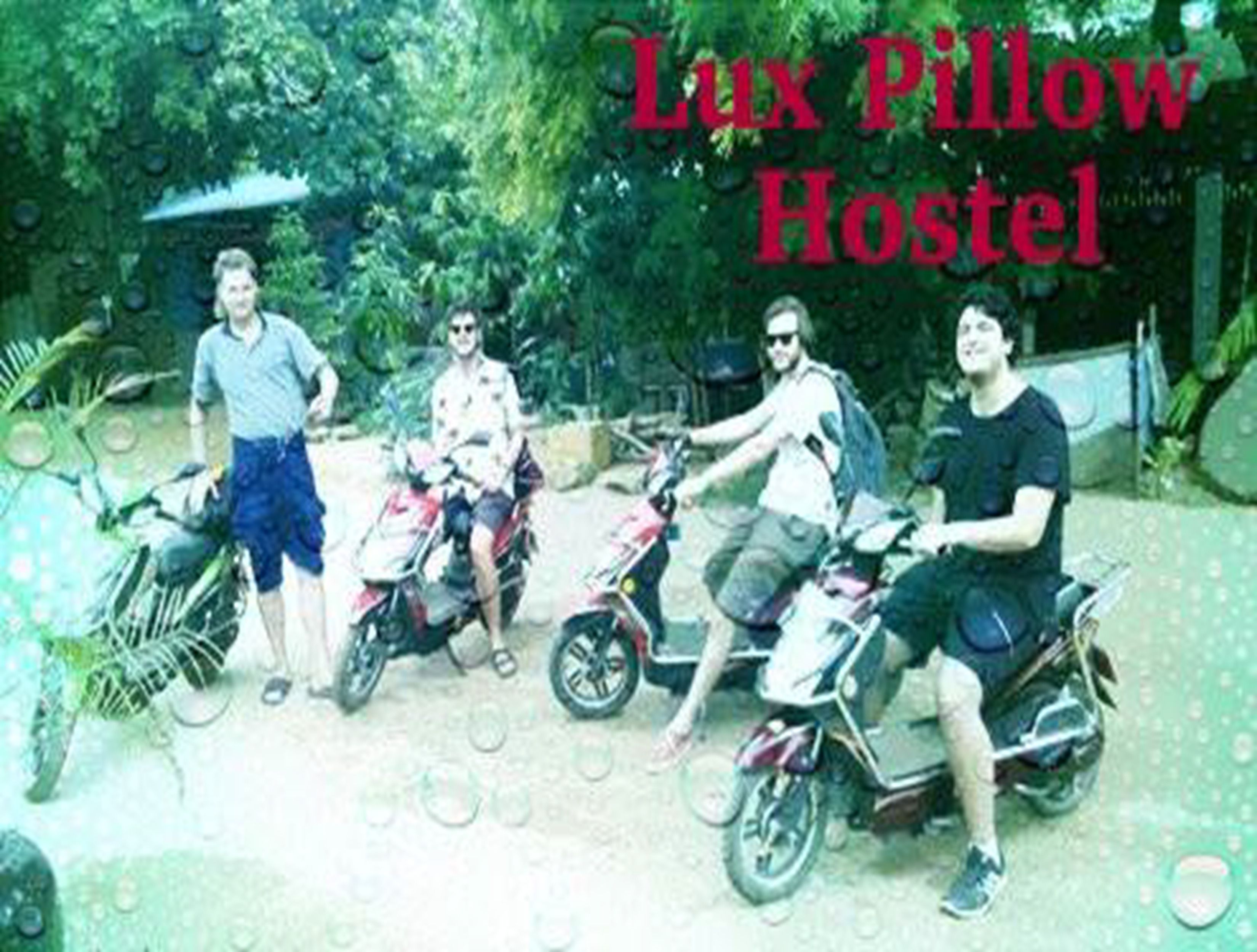 Four people on motorcycles, with a sign reading "Lux Pillow Hostel" in the background.