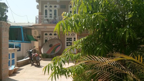 Un edificio con una gran rueda decorativa, una motocicleta estacionada adelante y abundante follaje.