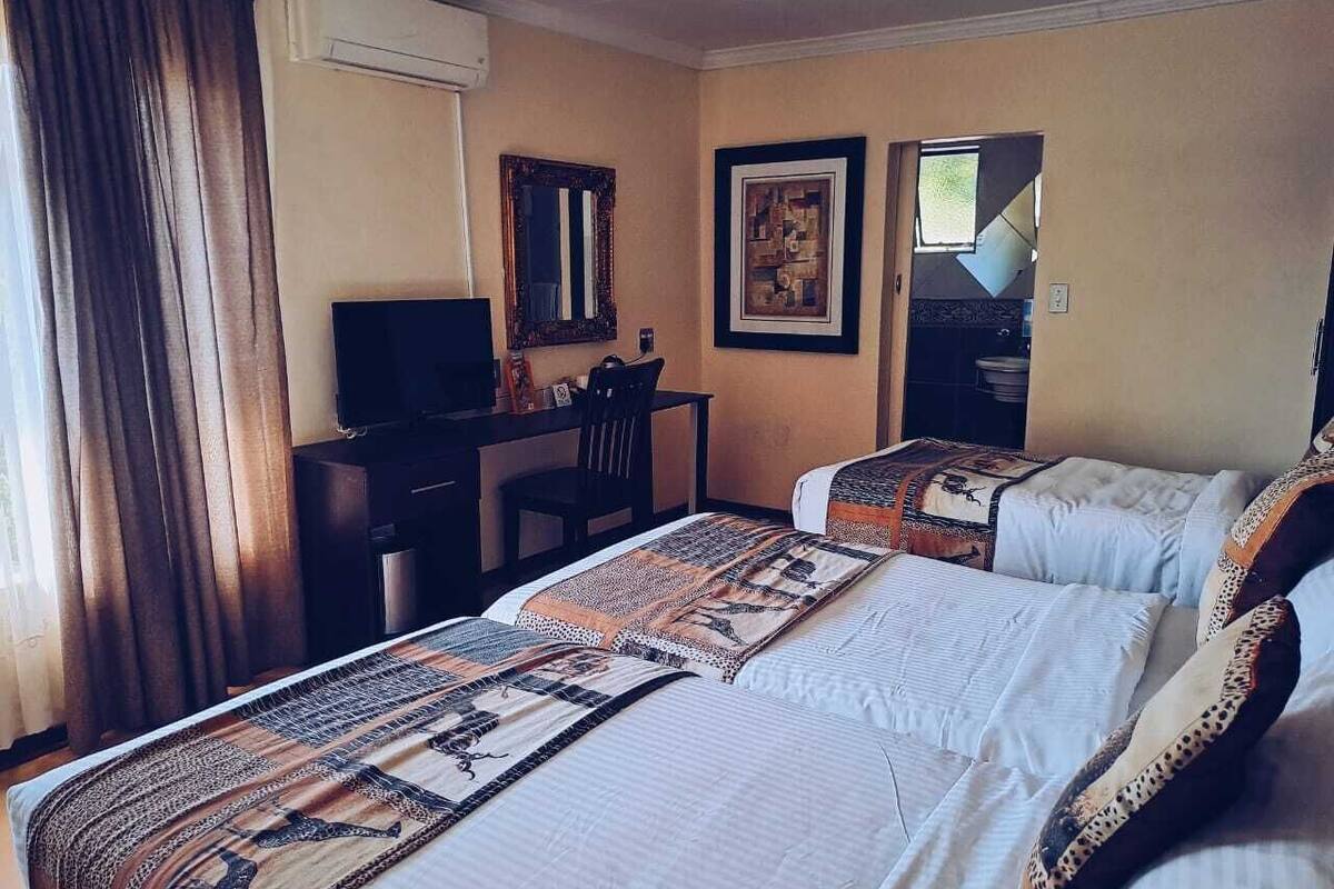 A hotel room with two beds, a desk, a chair, a television, and framed artwork on the walls.