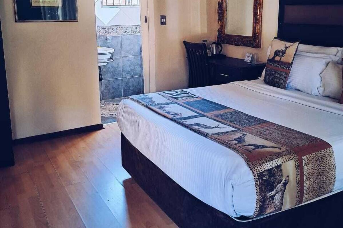 A bedroom with a large bed, a wooden floor, a bathroom with a window, and a mirror on the wall.