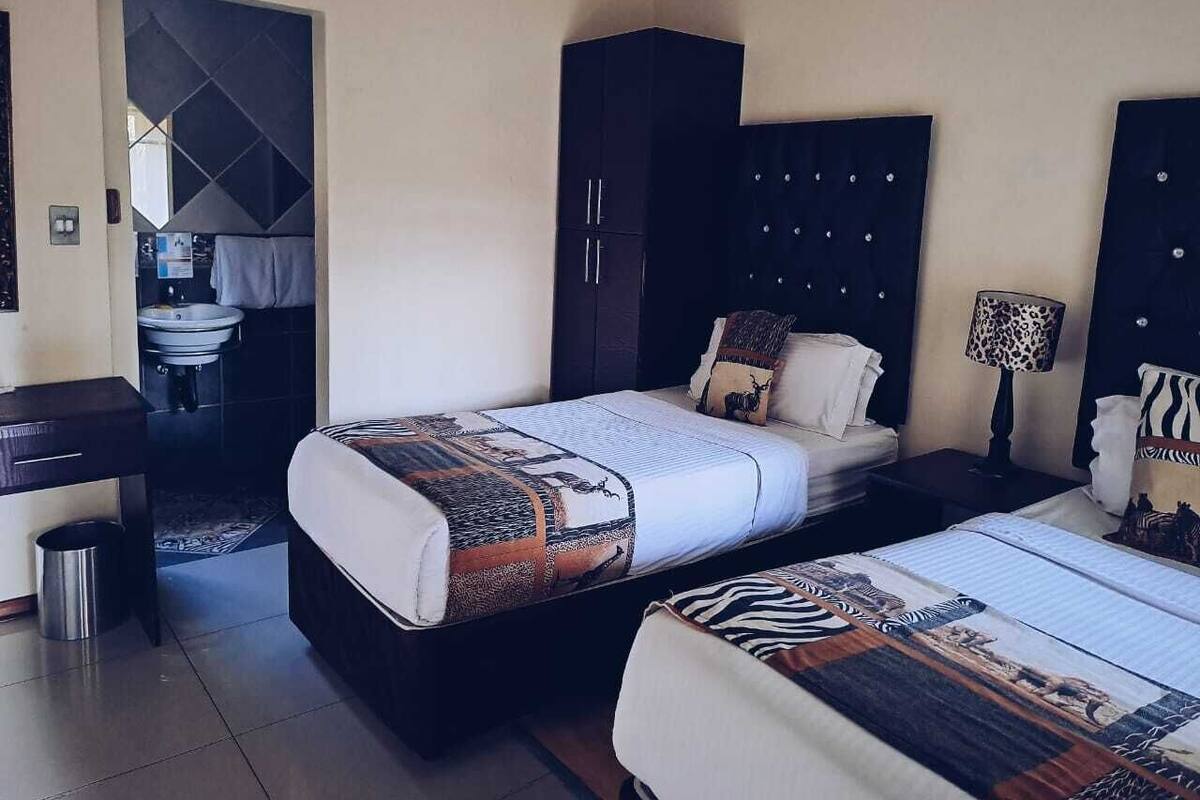 A hotel room with two beds, a wardrobe, a desk, and a bathroom visible through an open door.