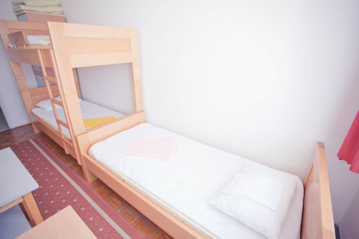 Ein Stockbett mit unterem Bett und Einzelbett, ein kleiner Tisch und ein roter Teppich.