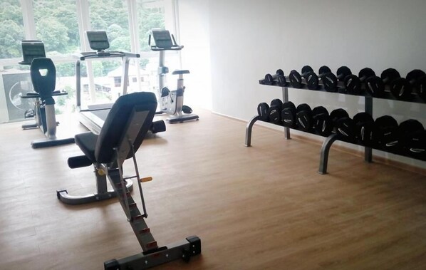 A gym with exercise equipment, a rowing machine, and a rack of dumbbells.