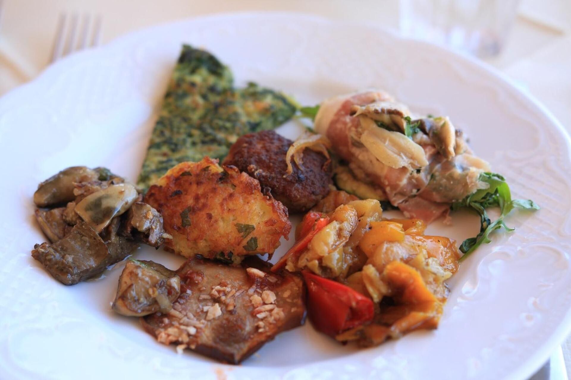 A plate with various dishes including a piece of fried food, a meat patty, and vegetables.