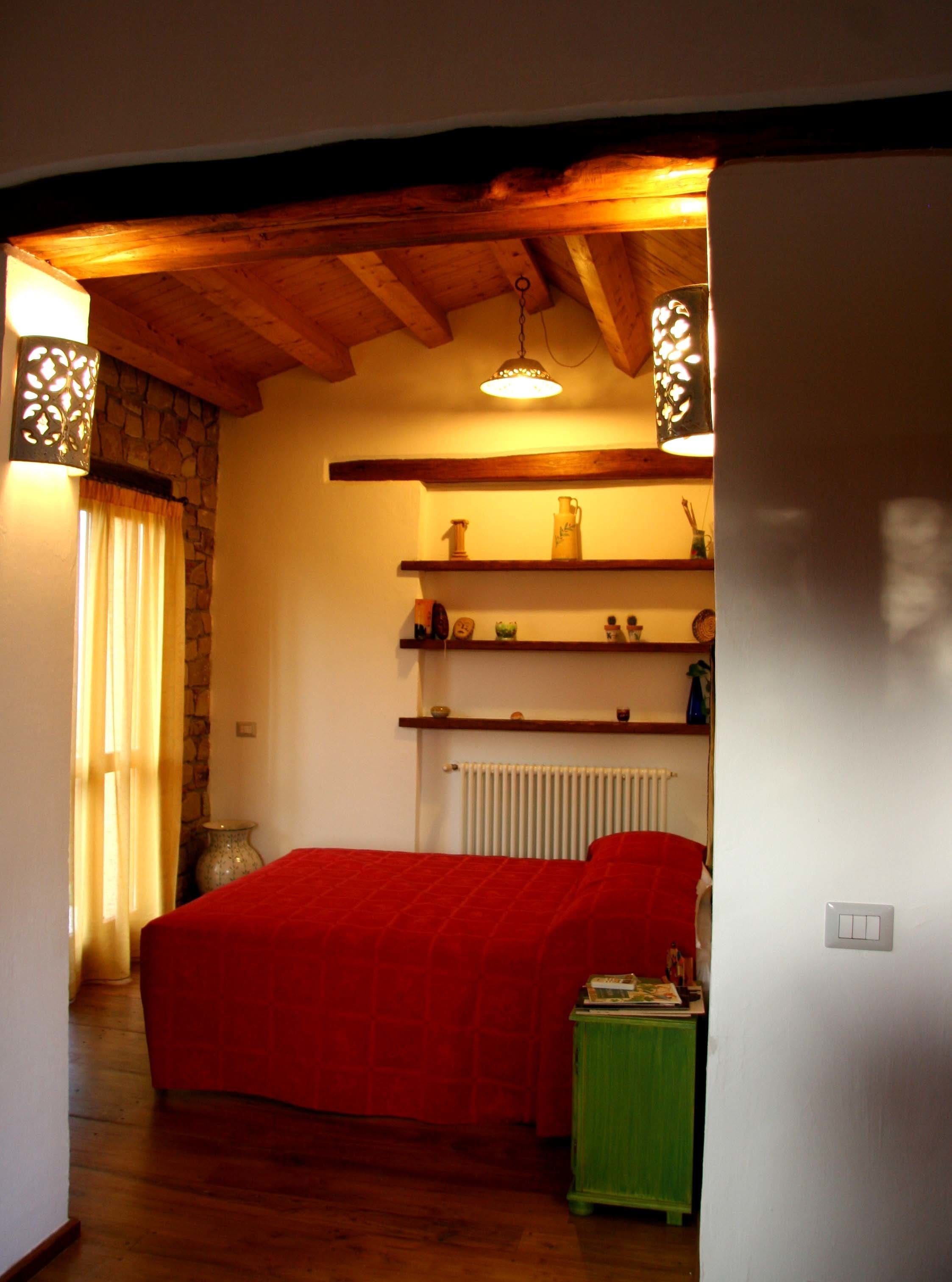 Une chambre confortable avec un plafond en bois, un lit rouge et des étagères ornées d’objets décoratifs.