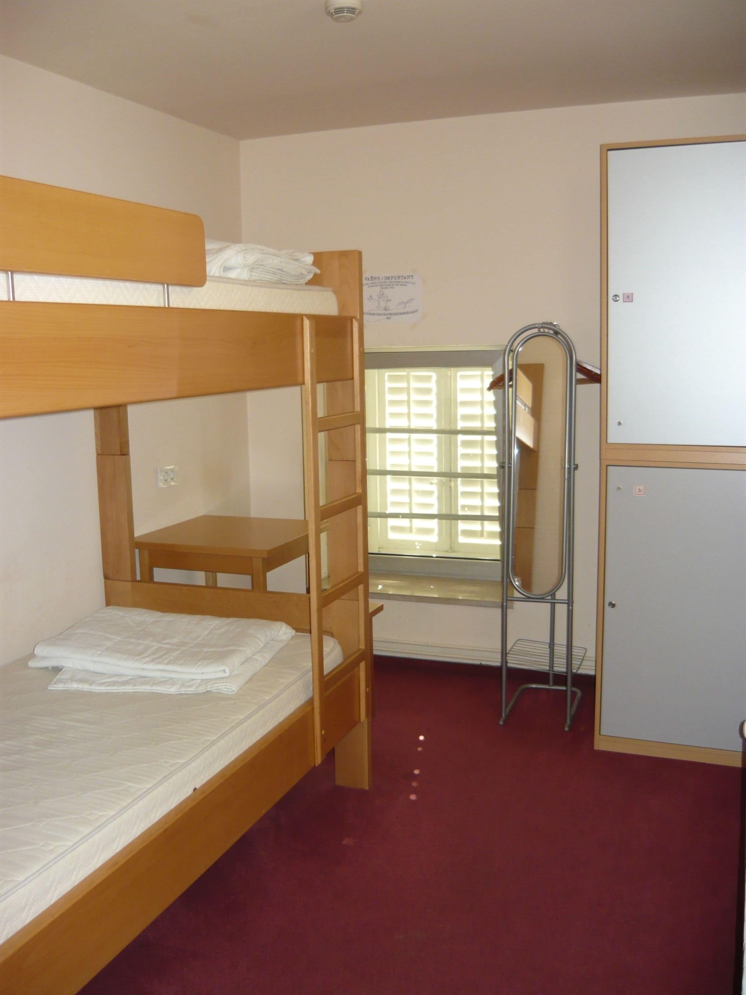 Une chambre avec un lit superposé, une petite table, un miroir et une armoire.