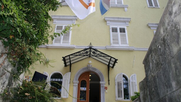 Un edificio con fachada amarilla, contraventanas blancas y una entrada central con un arco decorativo.