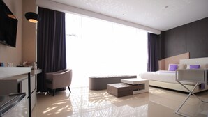 Una habitación de hotel moderna con un ventanal grande, una cama, un sofá, una mesa de centro y un escritorio con una silla.