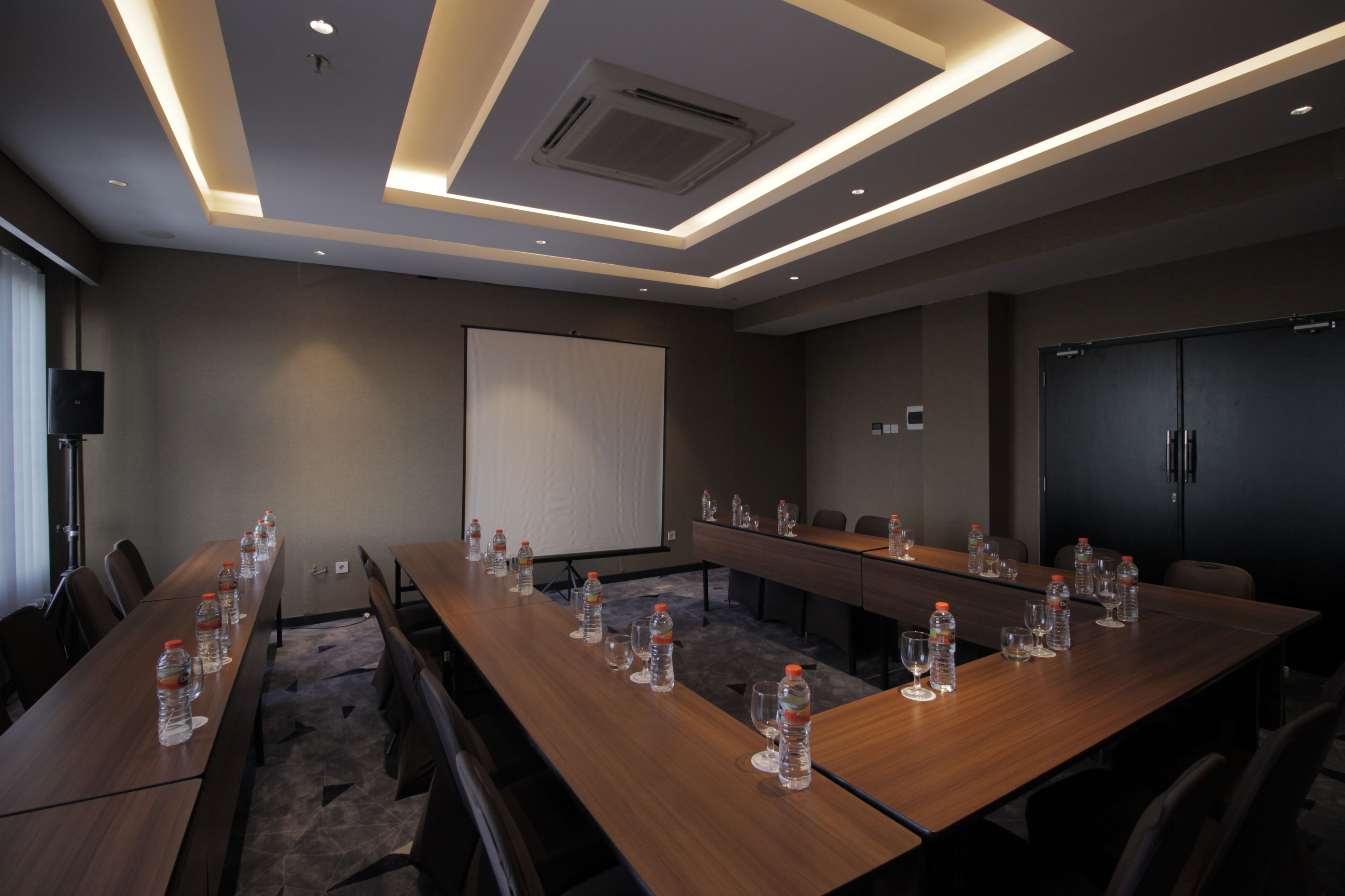 A conference room with a long table, chairs, water bottles, and a projector screen.