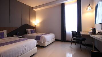 A hotel room with two beds, a desk, a chair, and a large window with curtains.