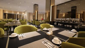 Un comedor moderno con mesas dispuestas para el servicio, sillas verdes y una zona de bar con copas.