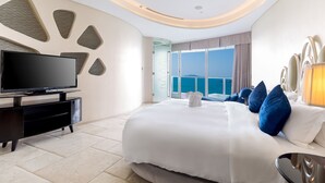 A modern hotel room with a large bed, a flat-screen TV, and a balcony with a view of the sea.