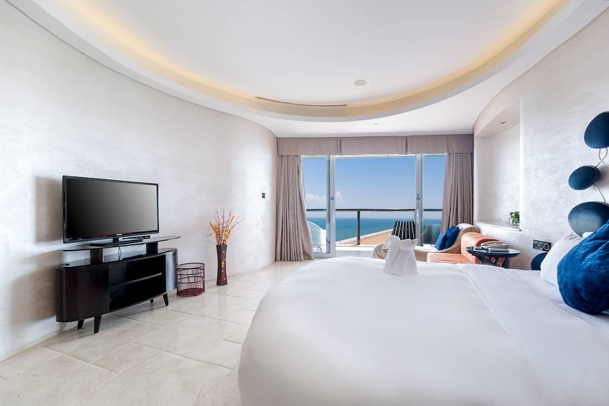 Habitació d'hotel moderna amb un llit gran, un televisor de pantalla plana, un balcó amb vista al mar i una zona d'estar decorada amb gust.