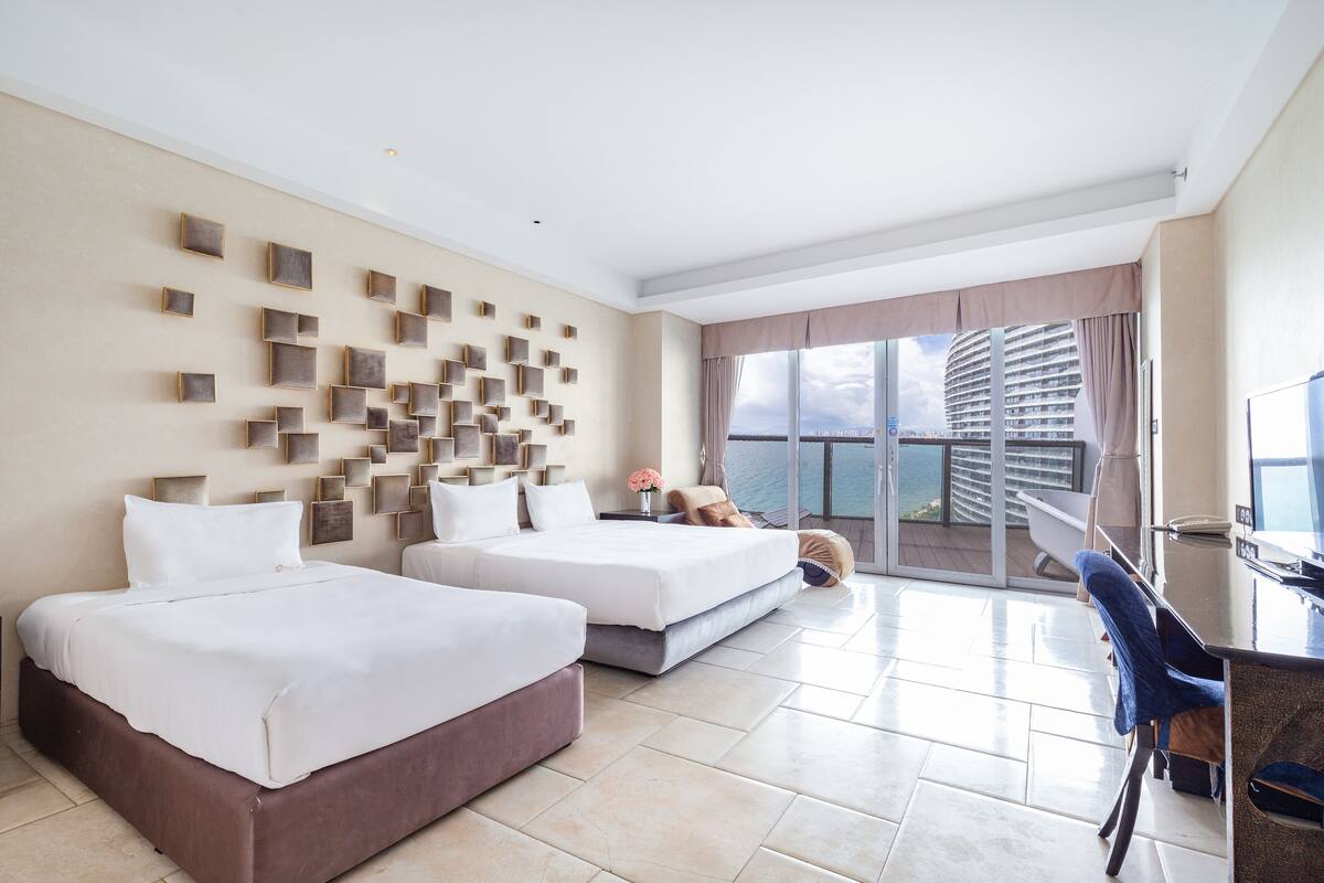 Habitació d'hotel amb dos llits, un escriptori i un balcó amb vista a un edifici.