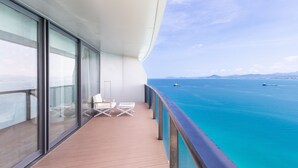 A balcony with glass walls, two white lounge chairs, and a view of the ocean with boats.