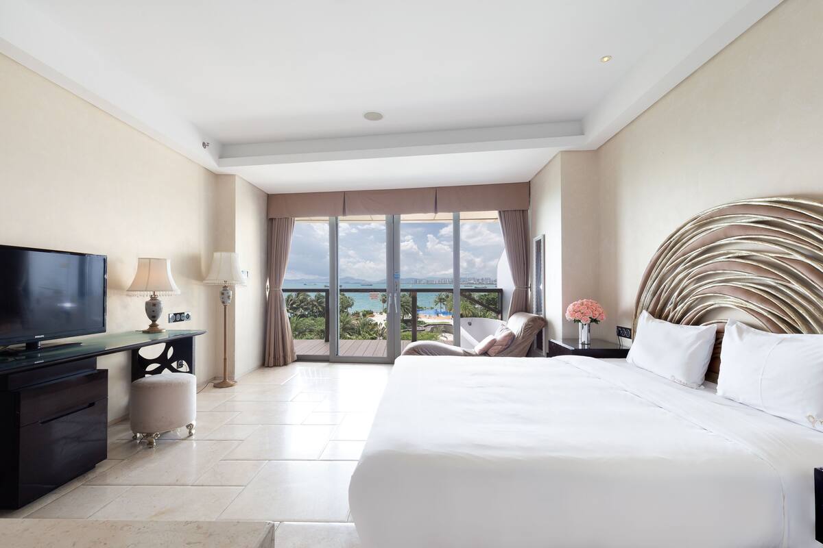 Habitació d'hotel amb un llit gran, una televisió, una taula de treball i vista a l'oceà.