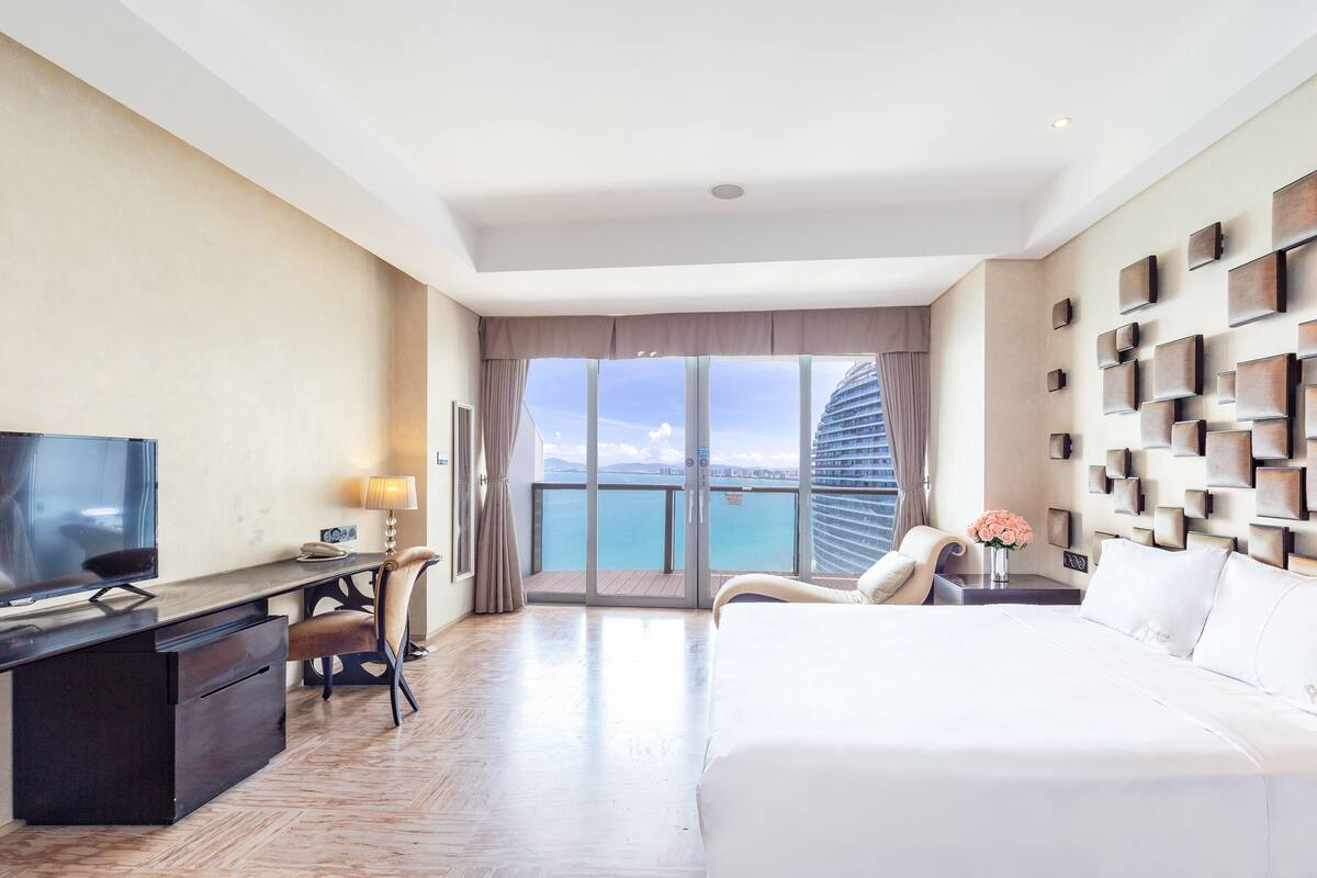 Habitació d'hotel moderna amb un llit gran, un escriptori amb televisió, una cadira i vistes al mar.