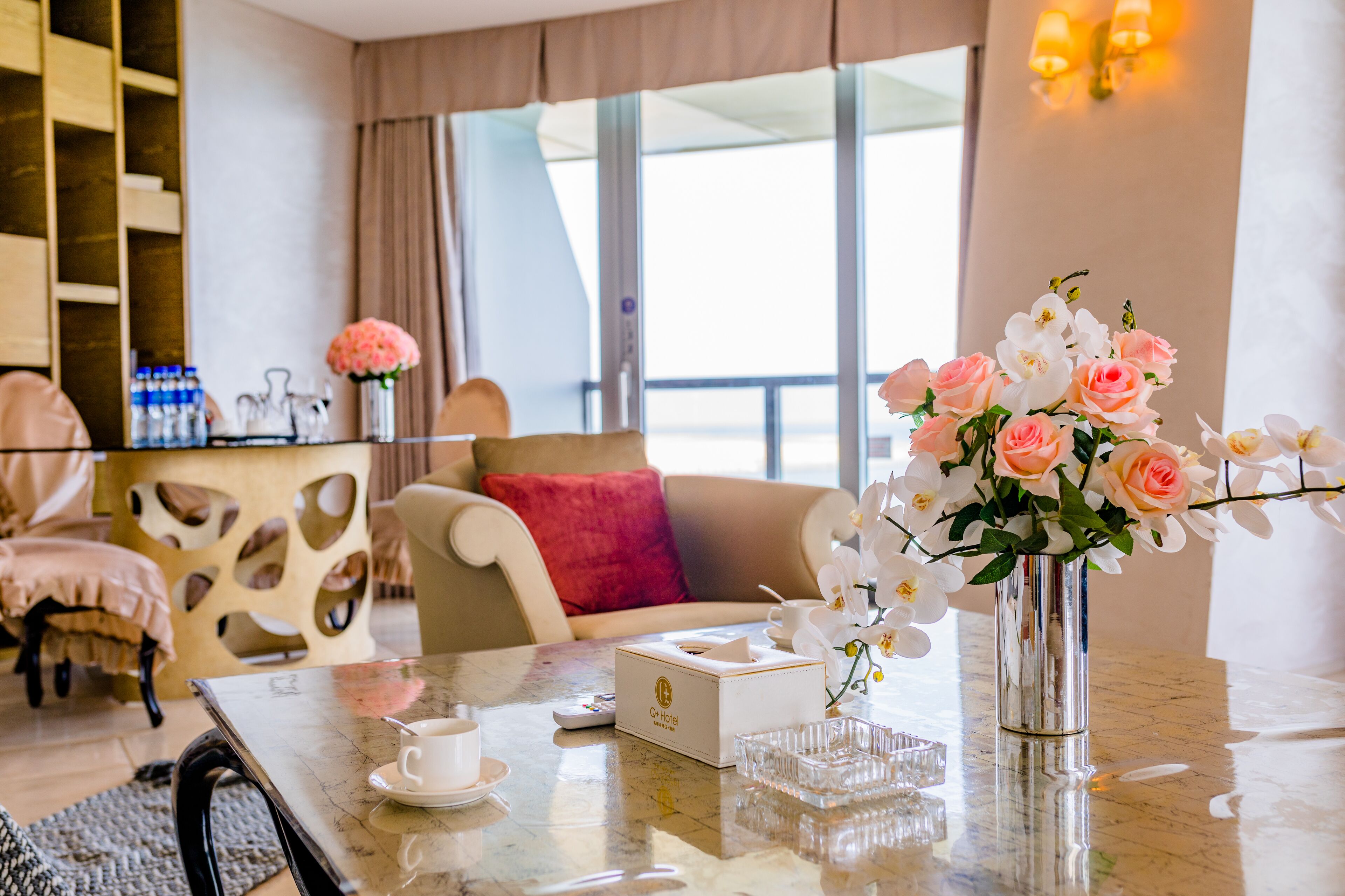 Habitación de hotel con una mesa de mármol, un jarrón de flores, un sofá con un cojín rojo y vistas al mar a través de amplias ventanas.