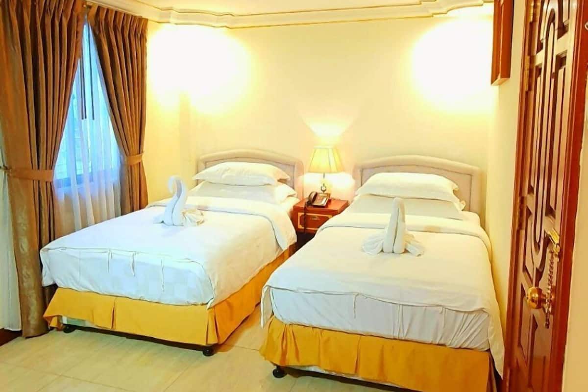 A hotel room with two beds, a wooden door, and a window with curtains.
