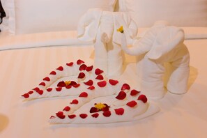 A bed with white linens and a decorative arrangement of rose petals and a small yellow flower. - Union Square Hotel (Yangon)