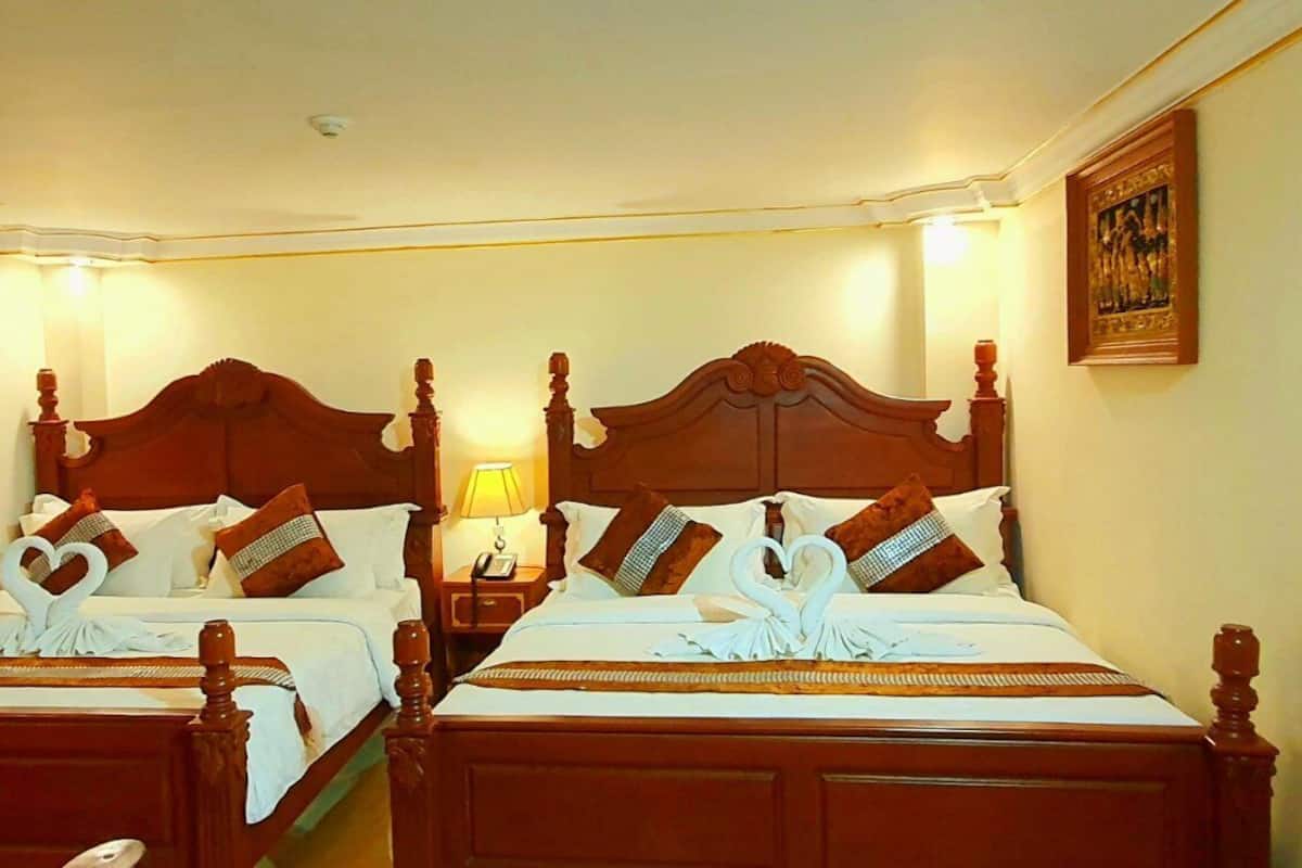 A hotel room with two wooden beds, each with a heart-shaped towel arrangement and matching pillows.