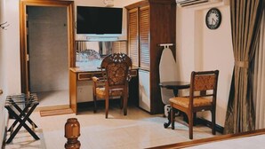 A room with a desk, two chairs, a television, a clock, and a window with curtains. - Union Square Hotel (Yangon)