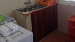 Uma cozinha pequena com pia, armários de madeira, uma janela e uma lixeira vermelha.