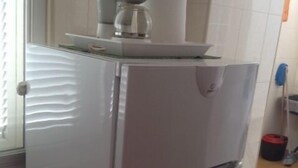Uma cozinha com geladeira branca, cafeteira e um rolo de papel toalha na bancada.