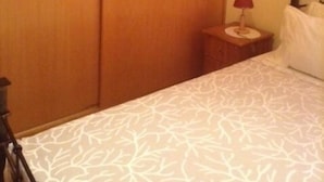Quarto de hotel com cama, mesa de cabeceira com abajur e guarda-roupa.