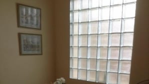 Uma sala de jantar com uma mesa de madeira redonda, quatro cadeiras, um vaso de flores e uma janela com persianas.