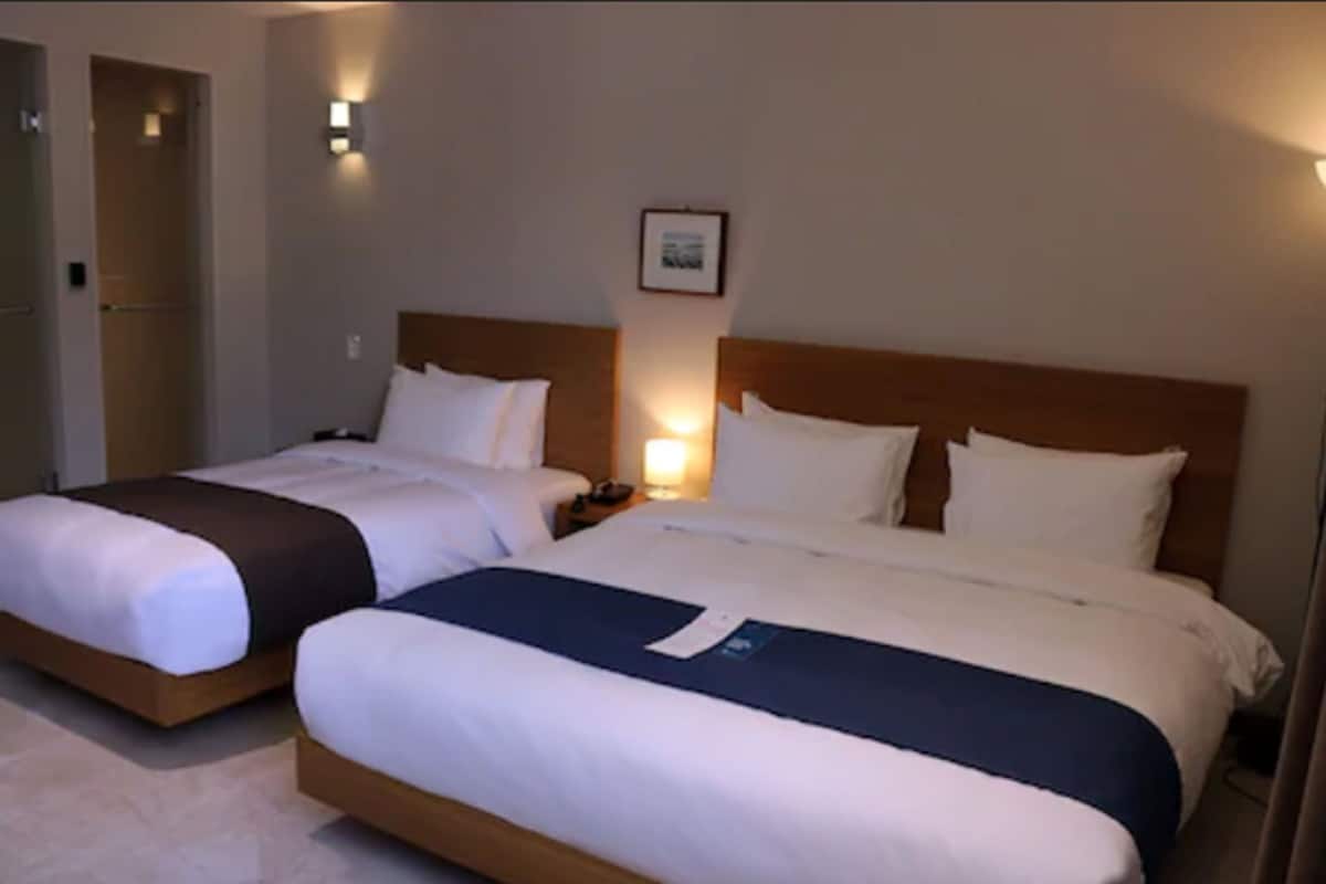 A hotel room with two beds, each with white bedding and a wooden headboard. There is a framed picture on the wall above the beds.