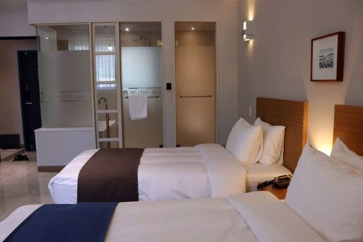 A hotel room with two beds, a wardrobe, and a bathroom with a shower and toilet.