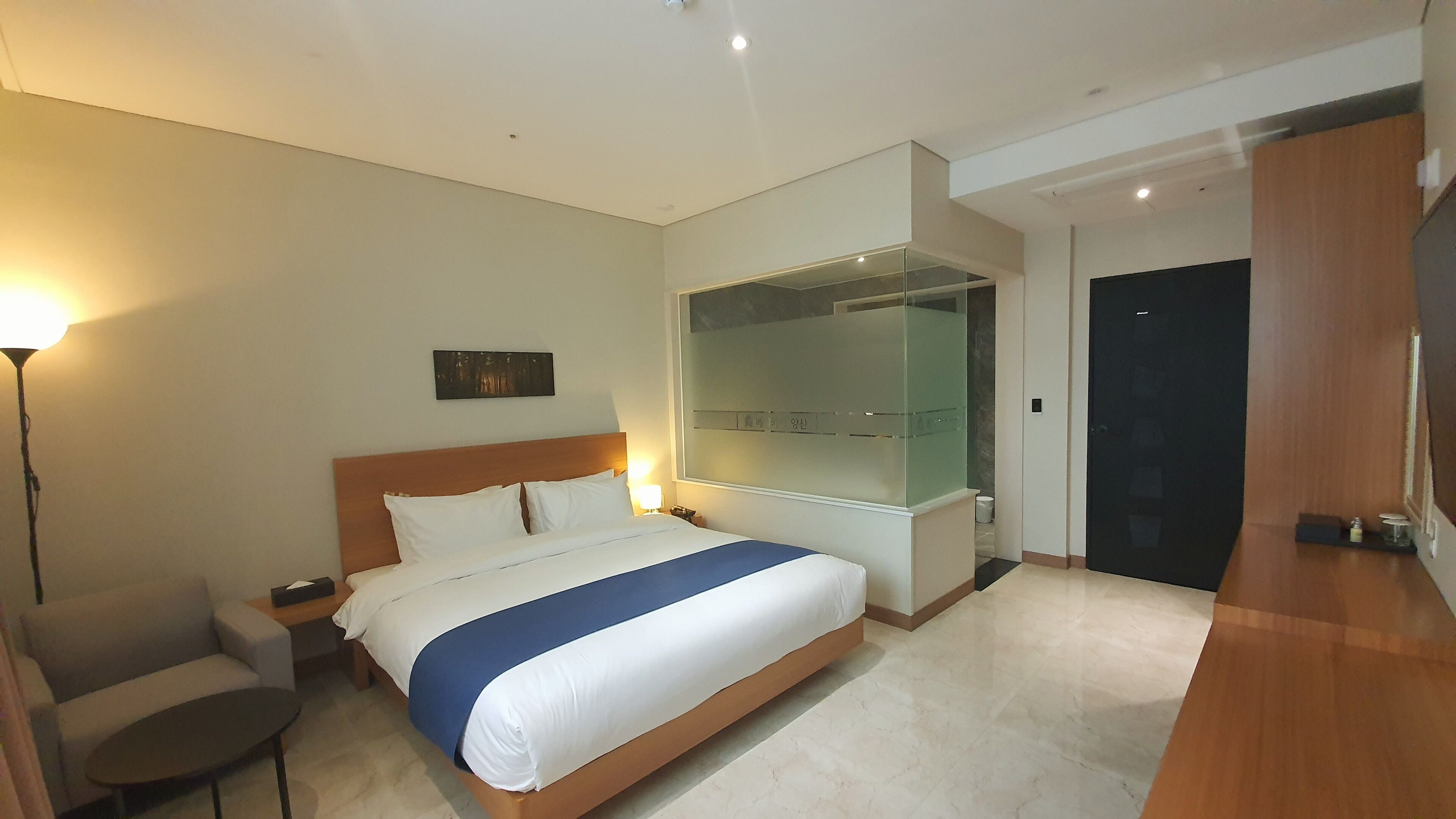 A hotel room with a bed, bedside table, lamp, and a large mirror.