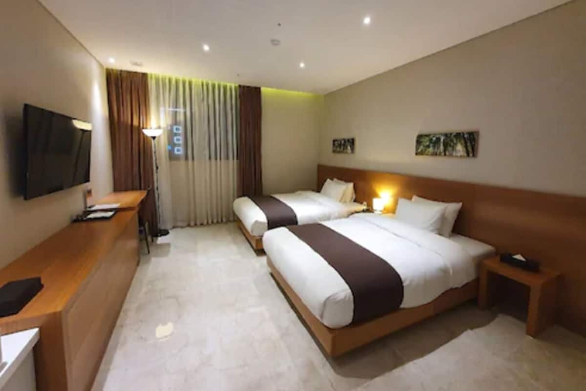 A hotel room with two beds, a desk, a TV, and a window with curtains.