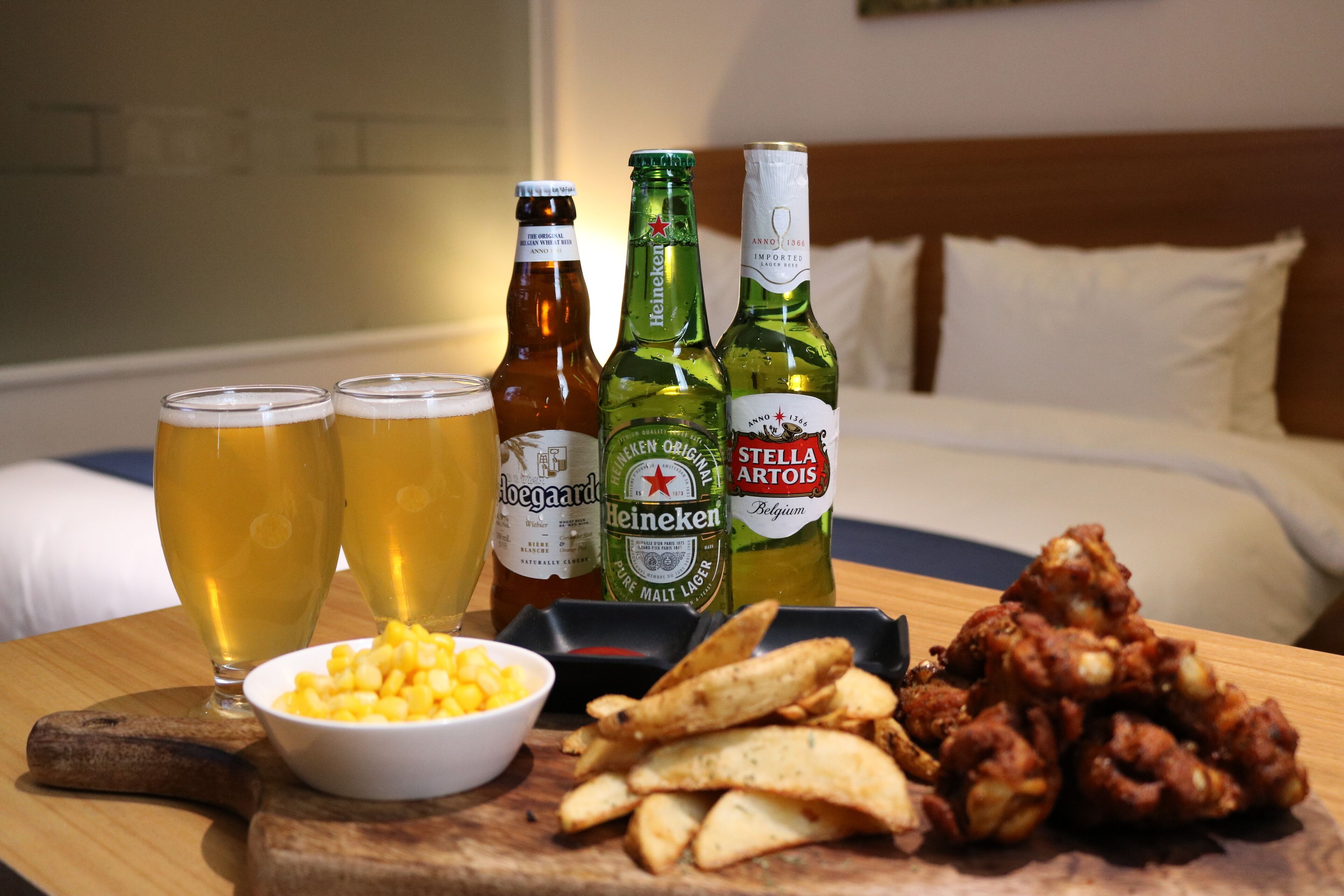 A wooden table with beer bottles, glasses, a bowl of corn, and fried food.