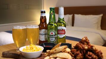 Una mesa de madera con botellas de cerveza, vasos, un bol de maíz y comida frita.
