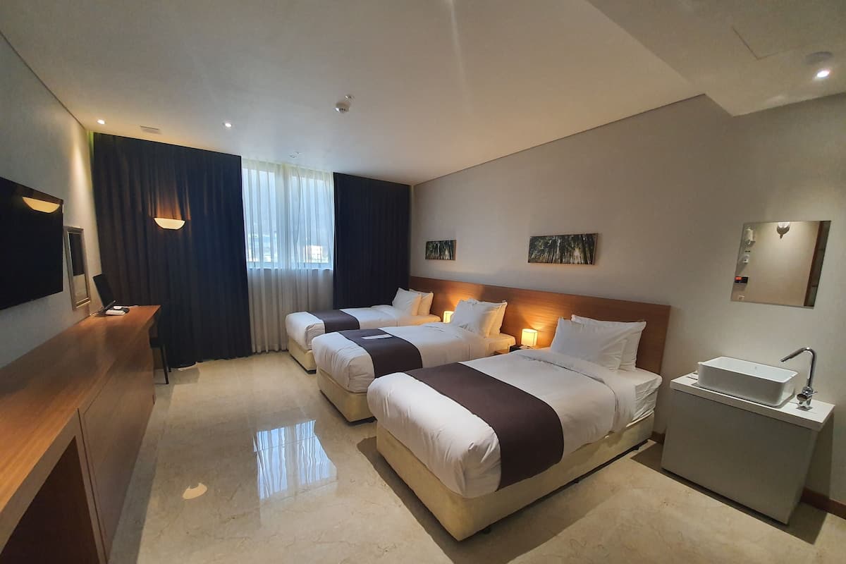 A hotel room with two beds, a desk, a bedside table, a sink, and a mirror.