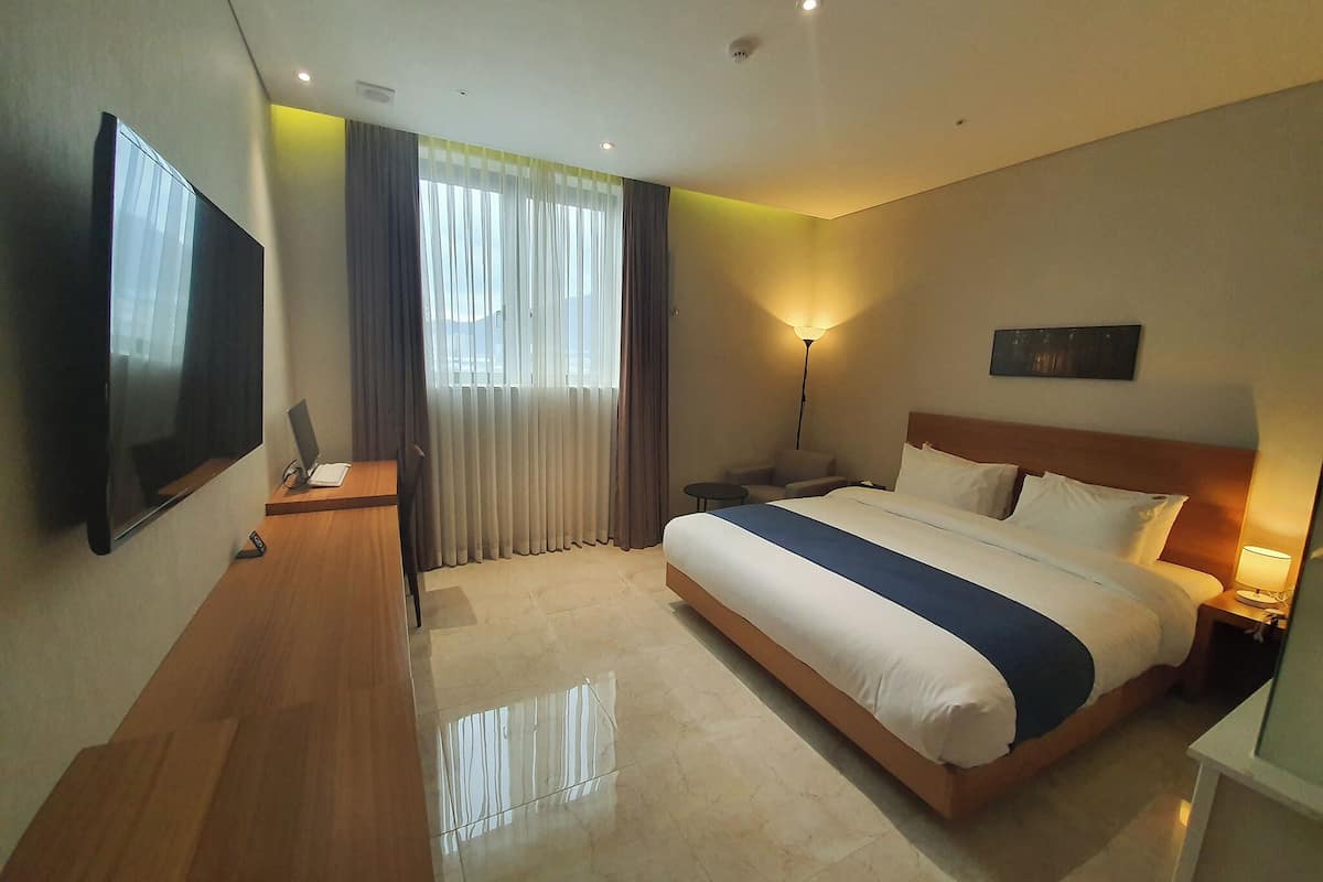 A hotel room with a bed, a desk, a TV, a lamp, and a window with curtains.