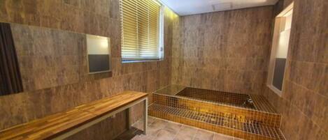 A modern bathroom with a wooden bench, a glass shower enclosure, and a large mirror.