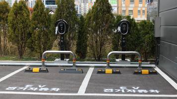 Ein Parkplatz mit Ladestationen für Elektrofahrzeuge, ausgewiesenen Stellplätzen und einer Stadtkulisse im Hintergrund.