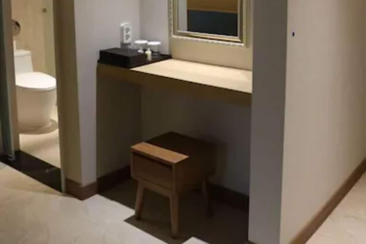 A bathroom with a toilet, a small wooden stool, a mirror, and a sink with a countertop.