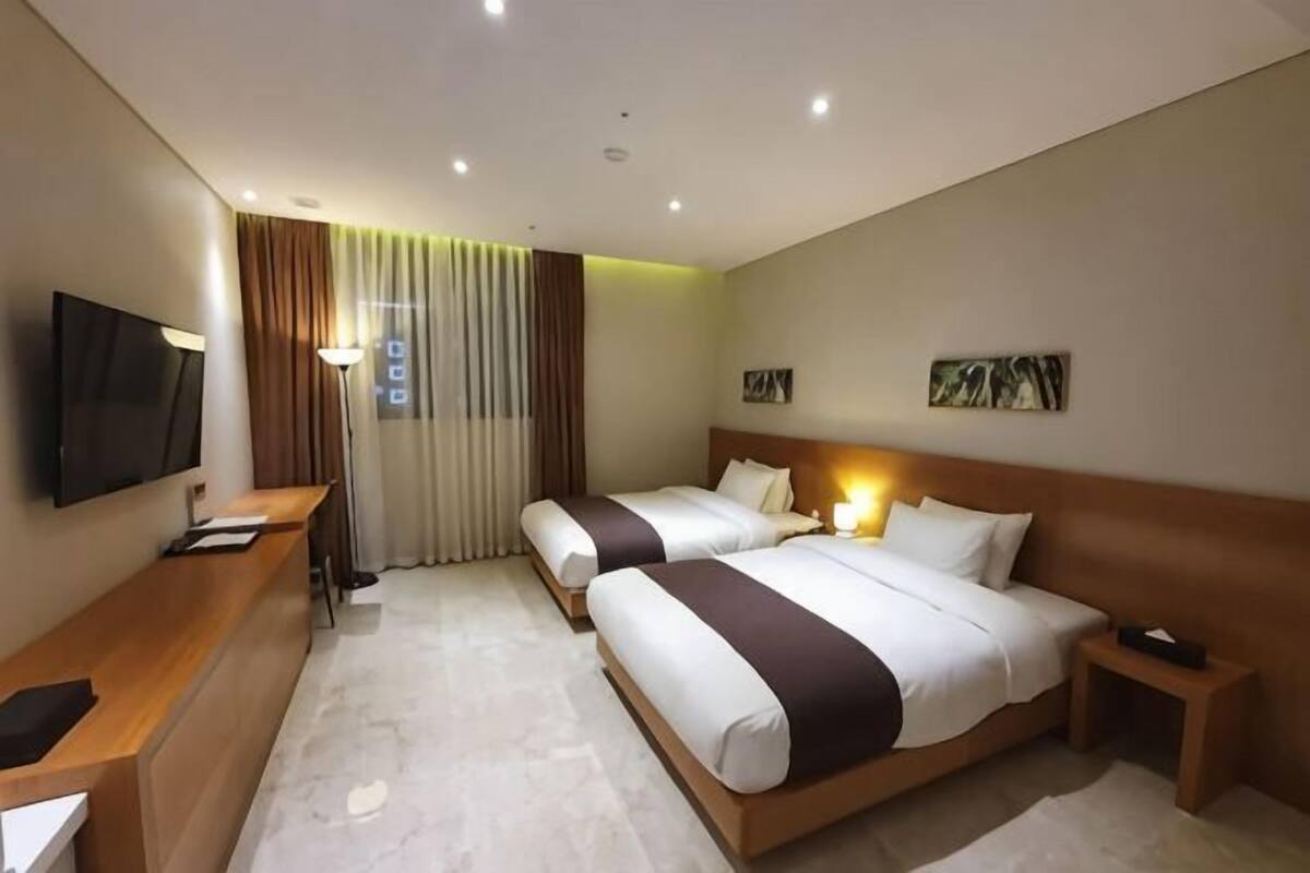 A hotel room with two beds, a desk, a TV, and a window with curtains.