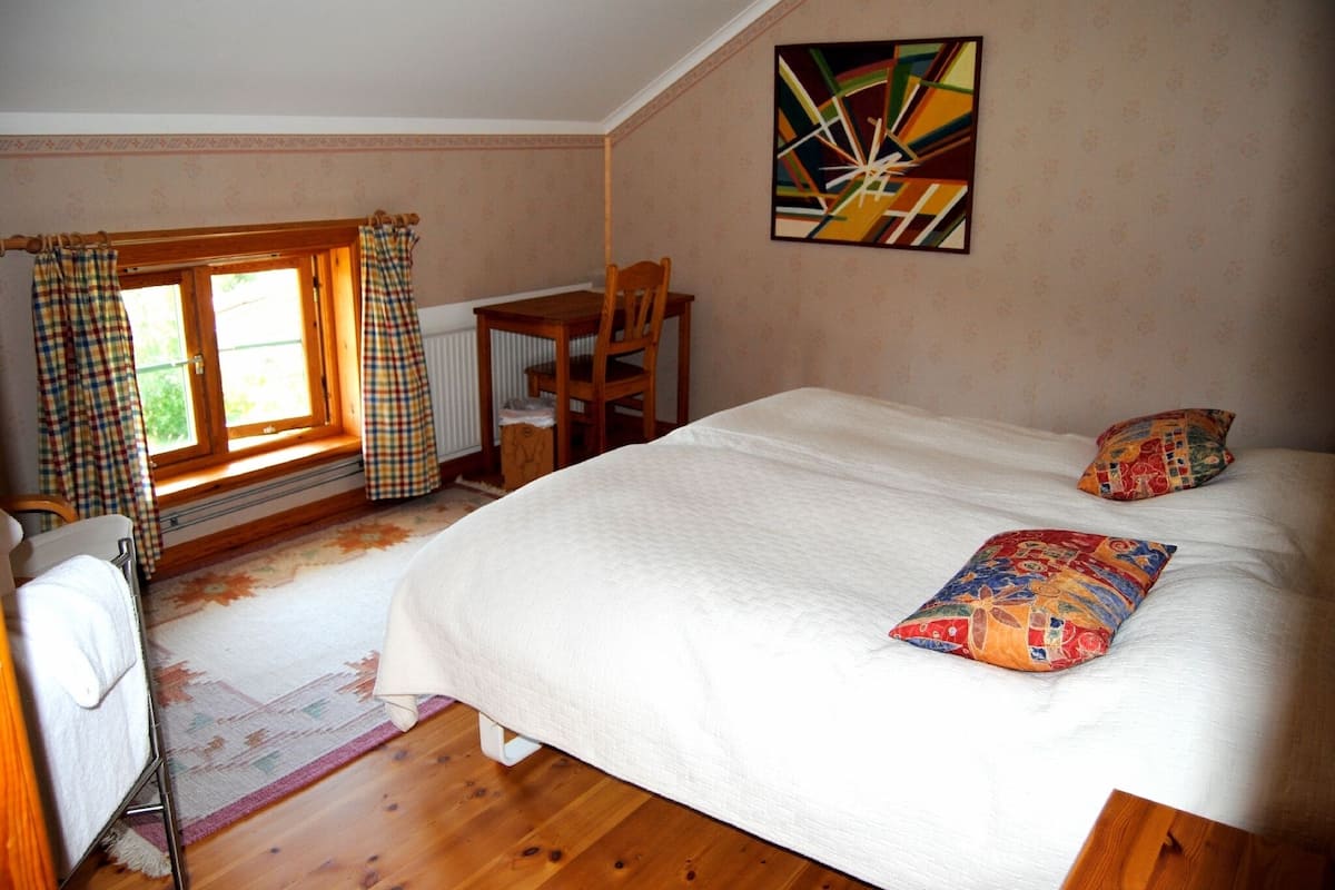 A bedroom with a bed, a chair, a table, and a window with curtains.