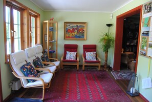 Une pièce avec deux fauteuils rouges, une bibliothèque en bois, un tableau encadré et un tapis rouge à motifs.