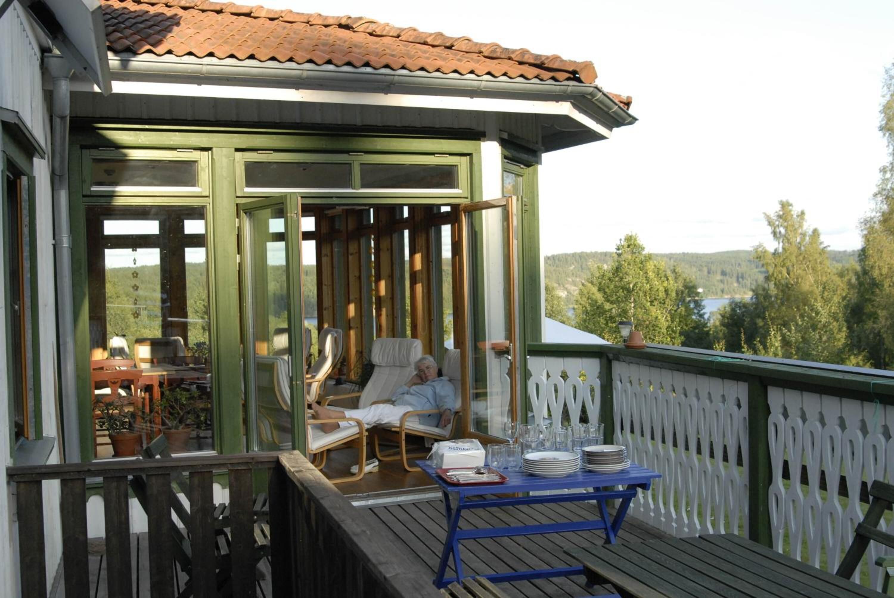 A covered outdoor area with a table set for dining, a lounge chair, and a view of the landscape.
