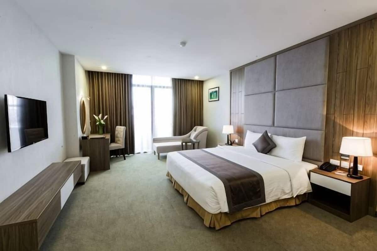 Habitación de hotel con cama, mesita de noche, lámpara, televisión y escritorio con silla.