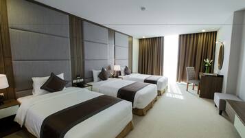 A hotel room with three beds, a desk, a chair, and a mirror.